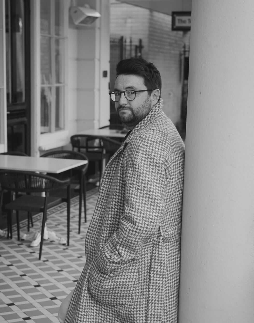 Man in a checked jacket standing in a shop doorway.