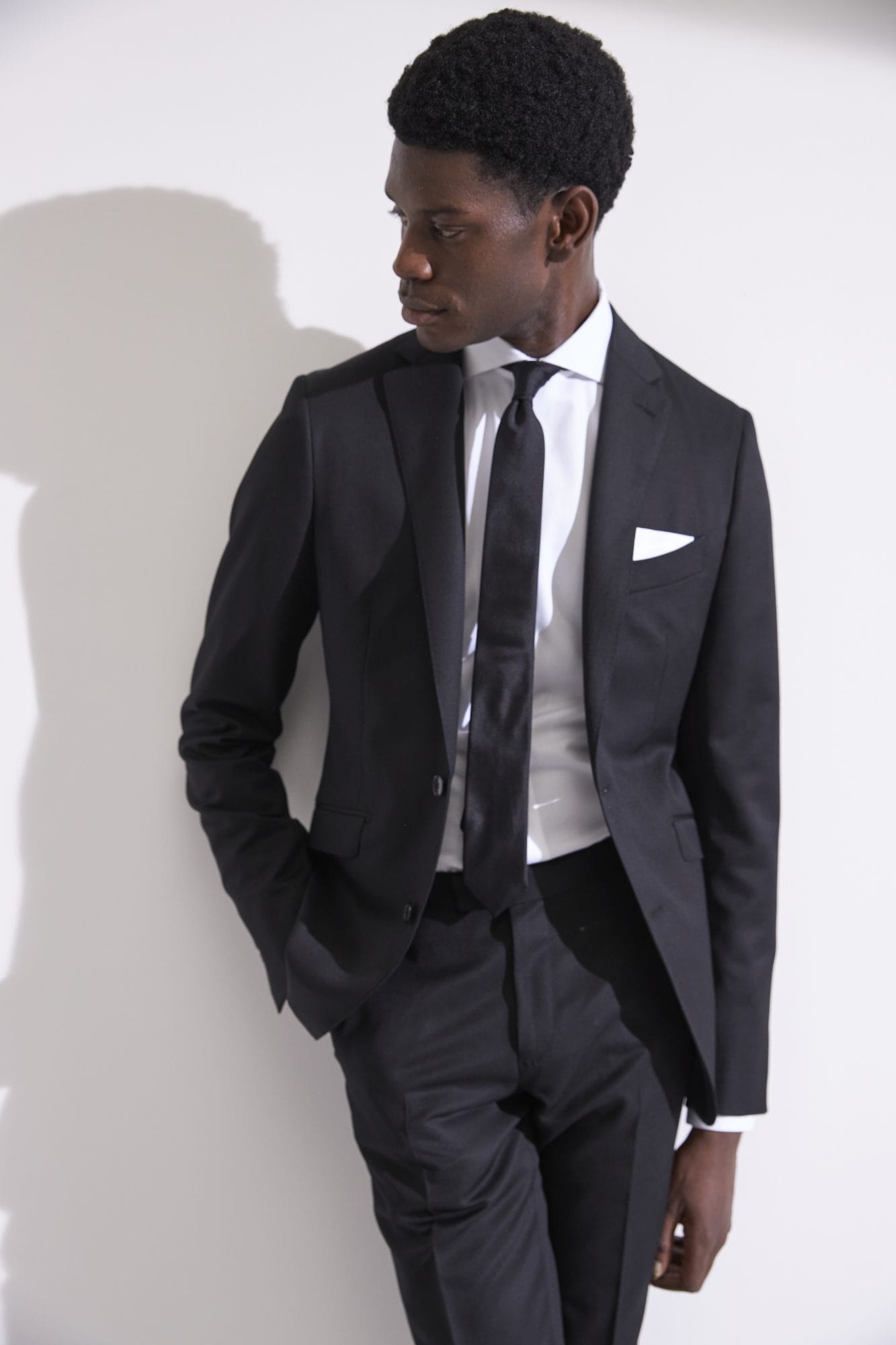 Man in black suit and tie against white wall