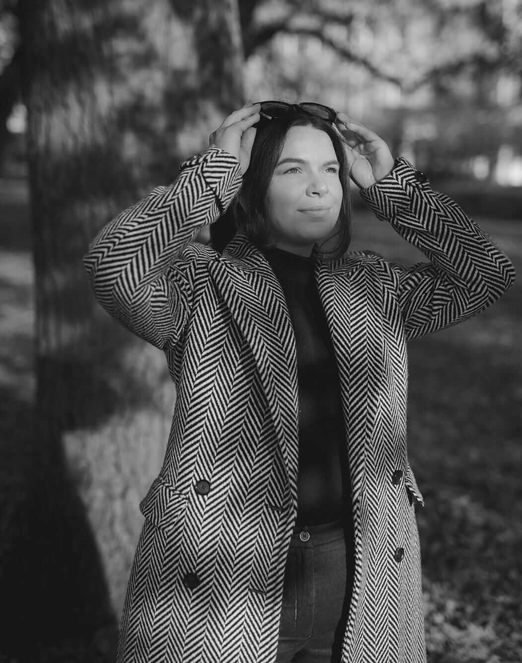 Woman in patterned coat adjusting sunglasses outdoors.
