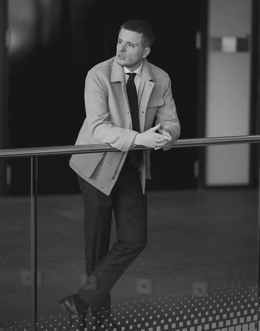 Man in light jacket and tie leaning on a railing.