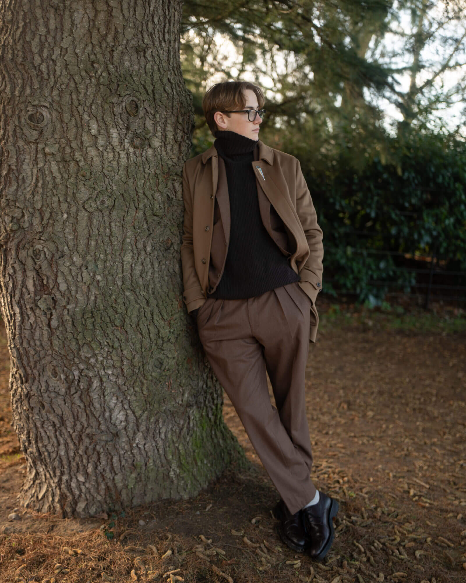 Man in brown tailoring leaning against a tree
