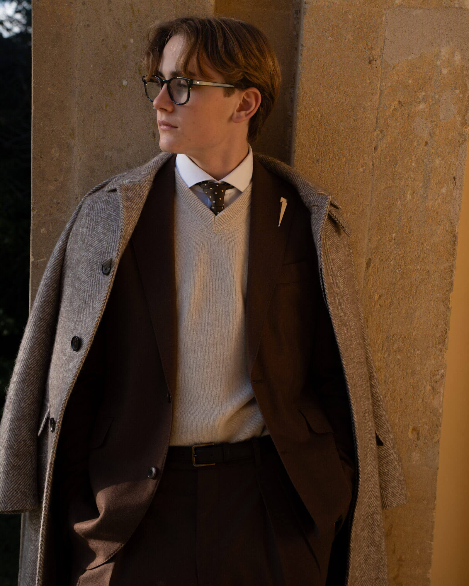 Man in layered tailoring standing by a stone wall