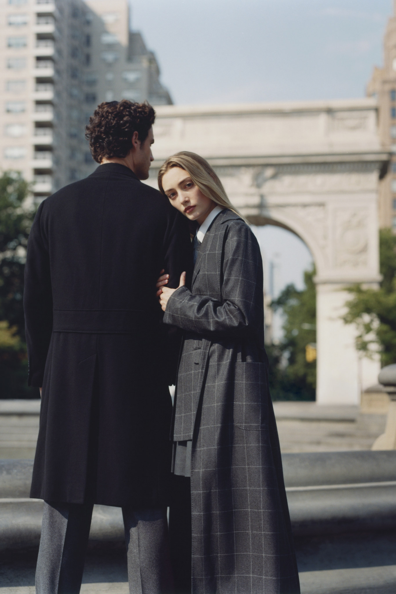 Male model in a long dark coat and female model in a grey check coat by the Washington Square Arch, New York
