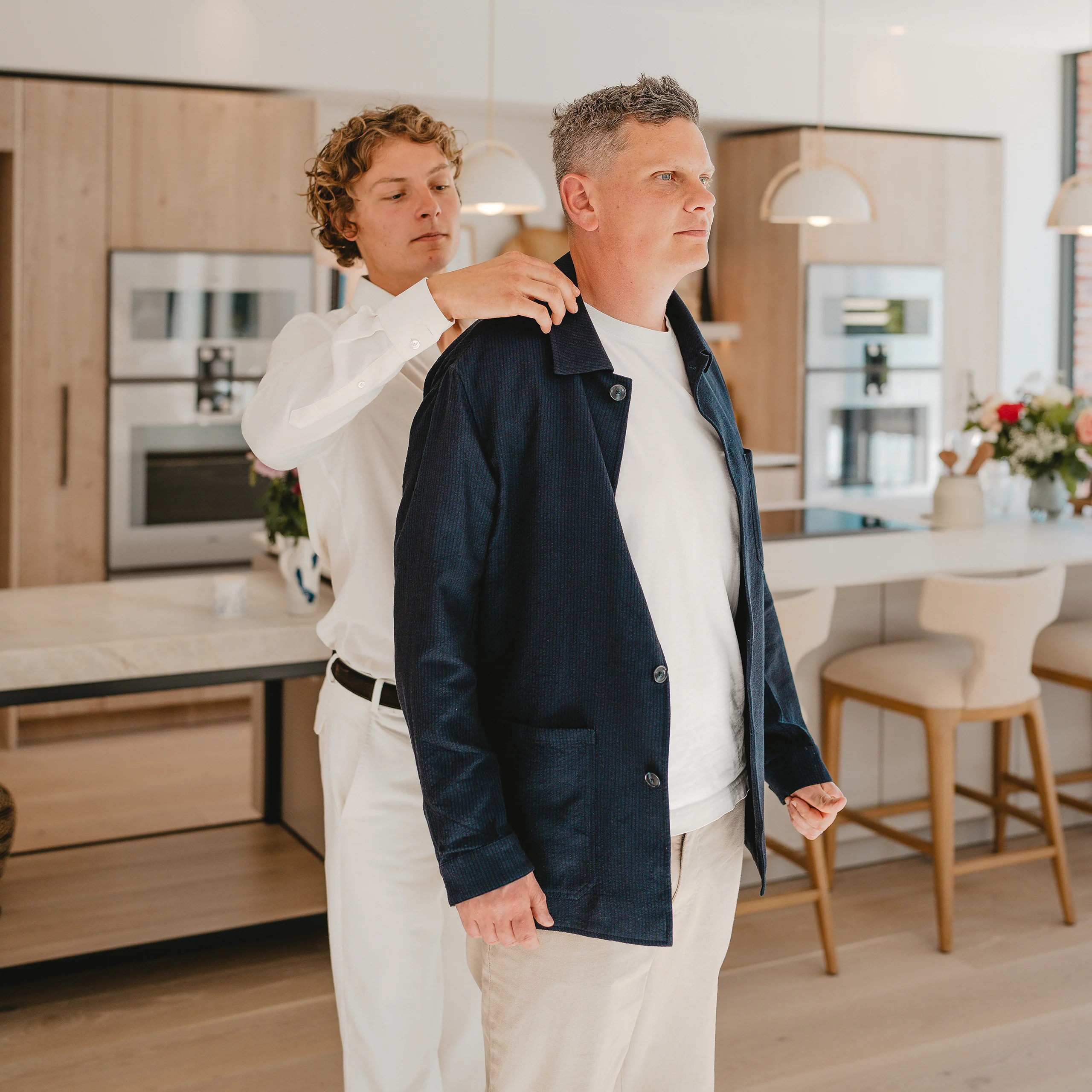 Clements and Church tailor adjusting a navy jacket at a client fitting in a bright kitchen