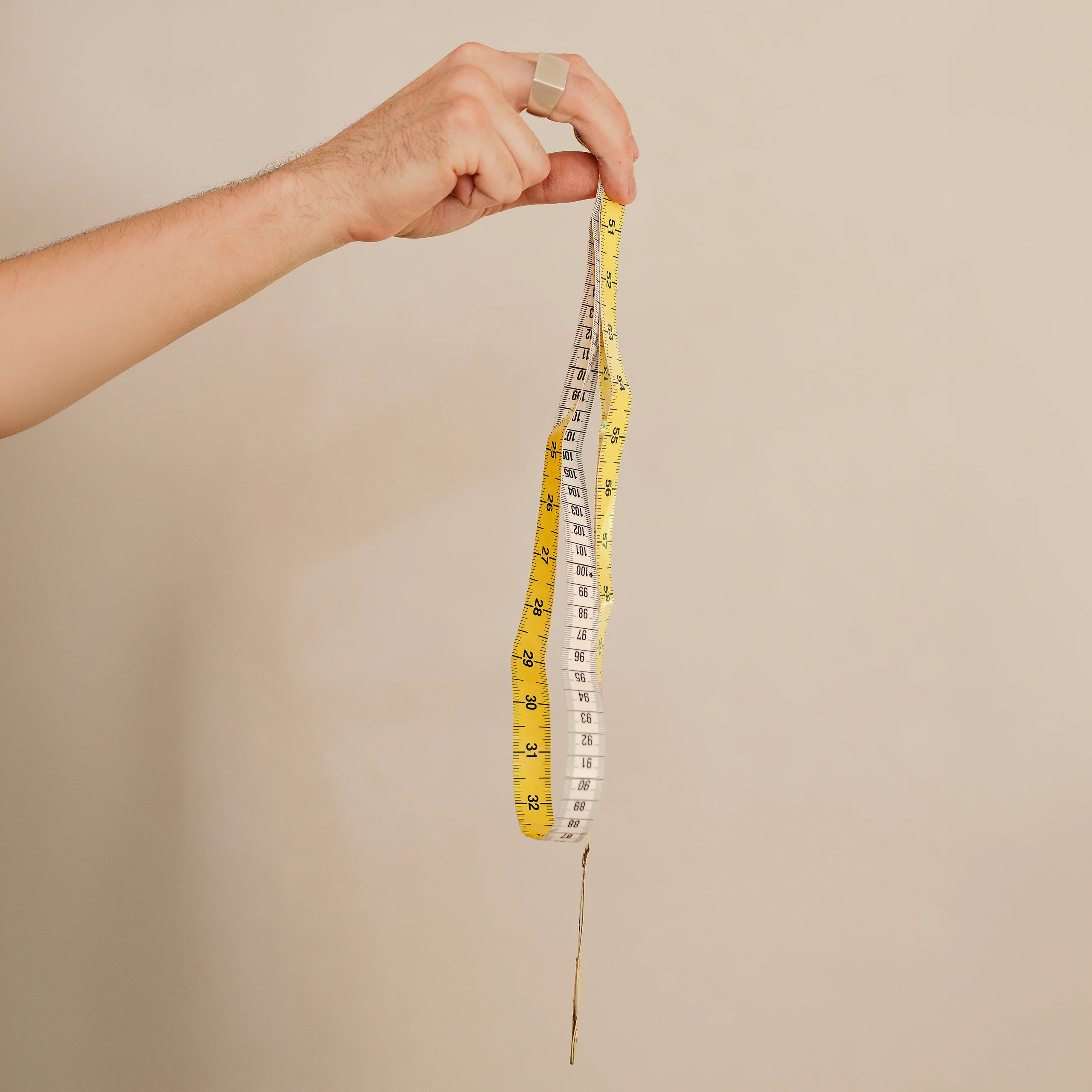 A hand holding a yellow tailor's tape measure against a warm stone wall