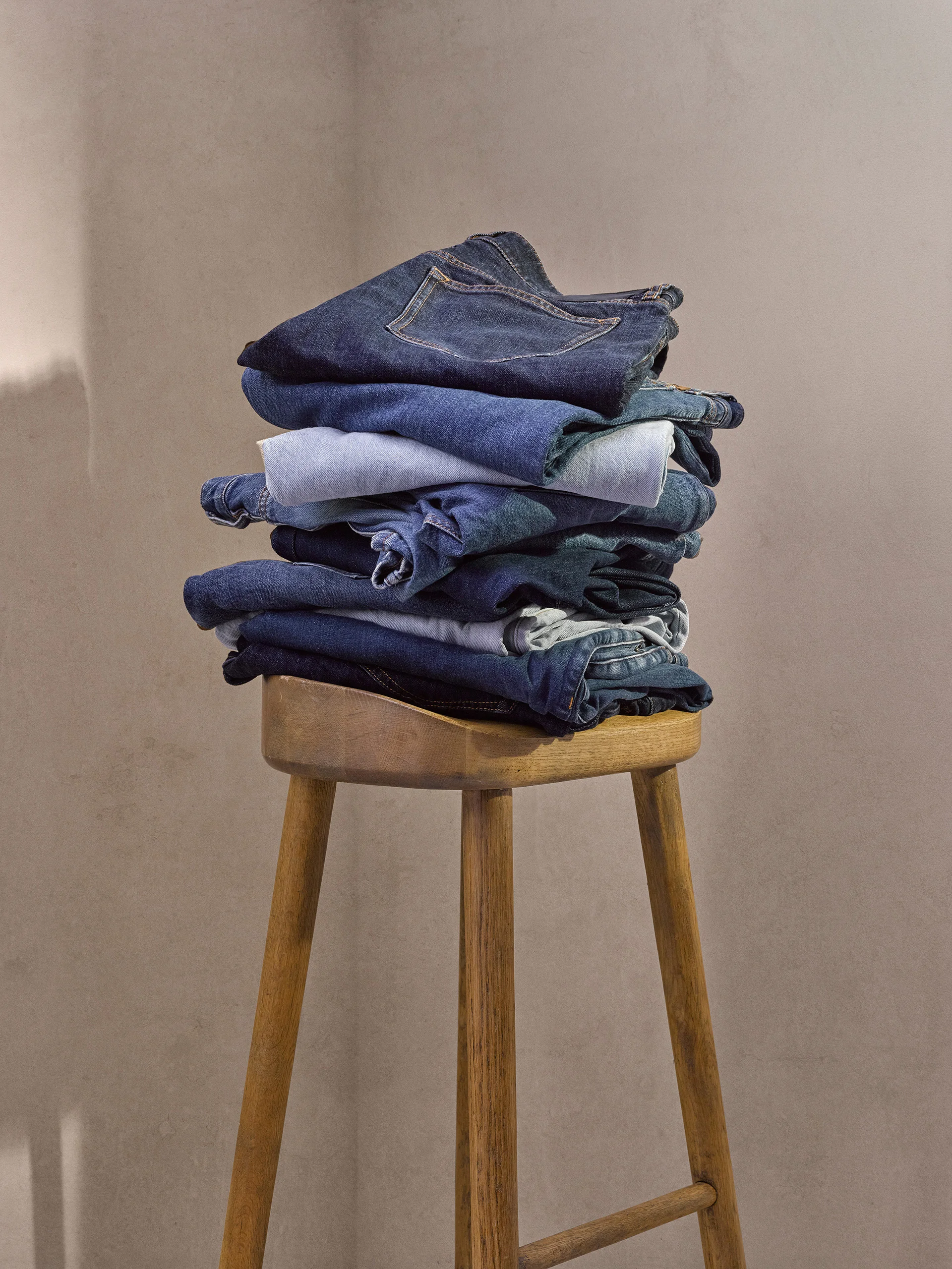 Stack of folded Clements and Church denim jeans on a tall wooden stool