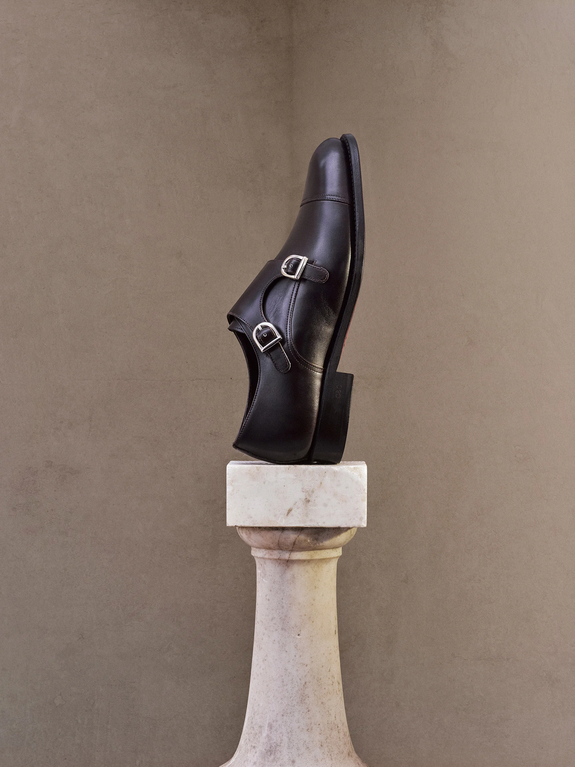Black leather double-monk shoe displayed on a stone balustrade