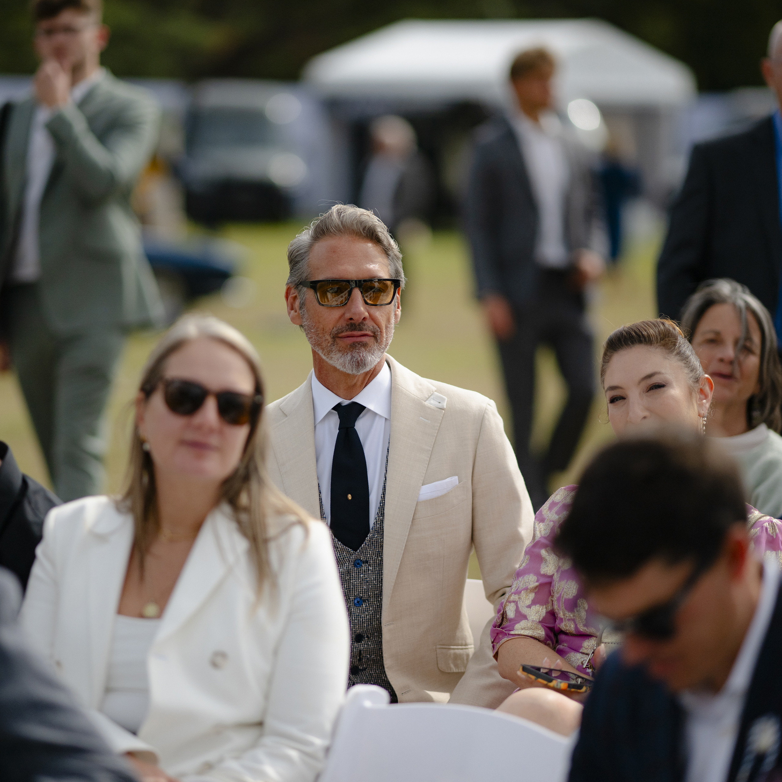 Guest in a cream tailored jacket, waistcoat and navy tie seated at the Salon Privé lawn