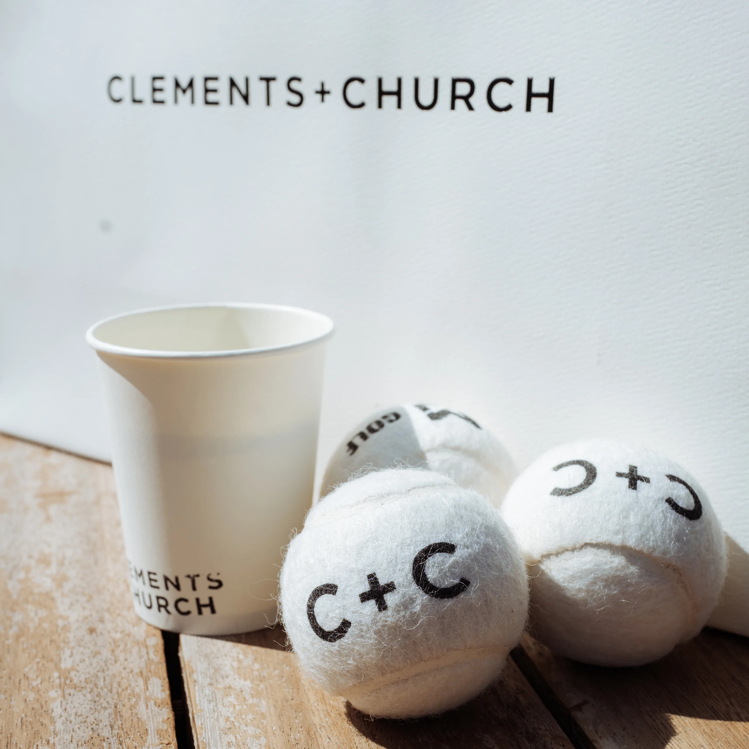 Clements + Church branded padel balls and coffee cup on a bench