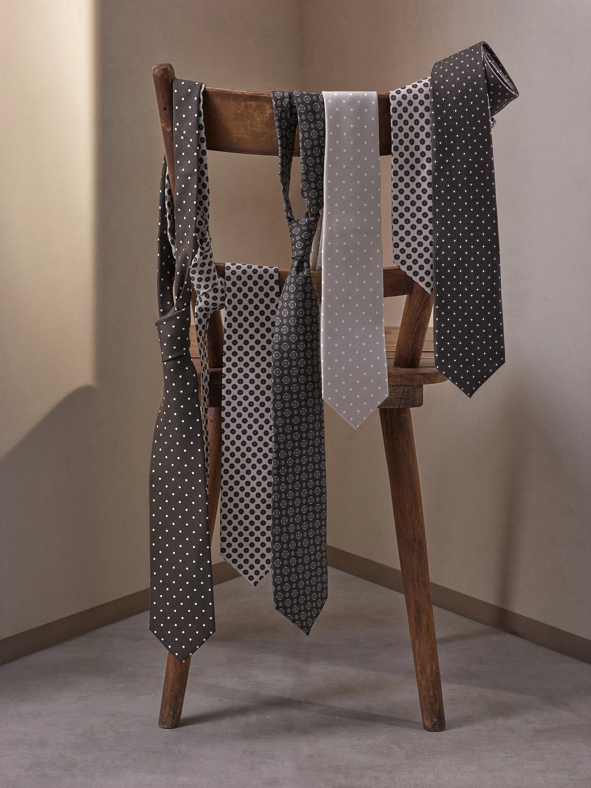 Five patterned silk ties in spot and geometric prints draped over a wooden chair