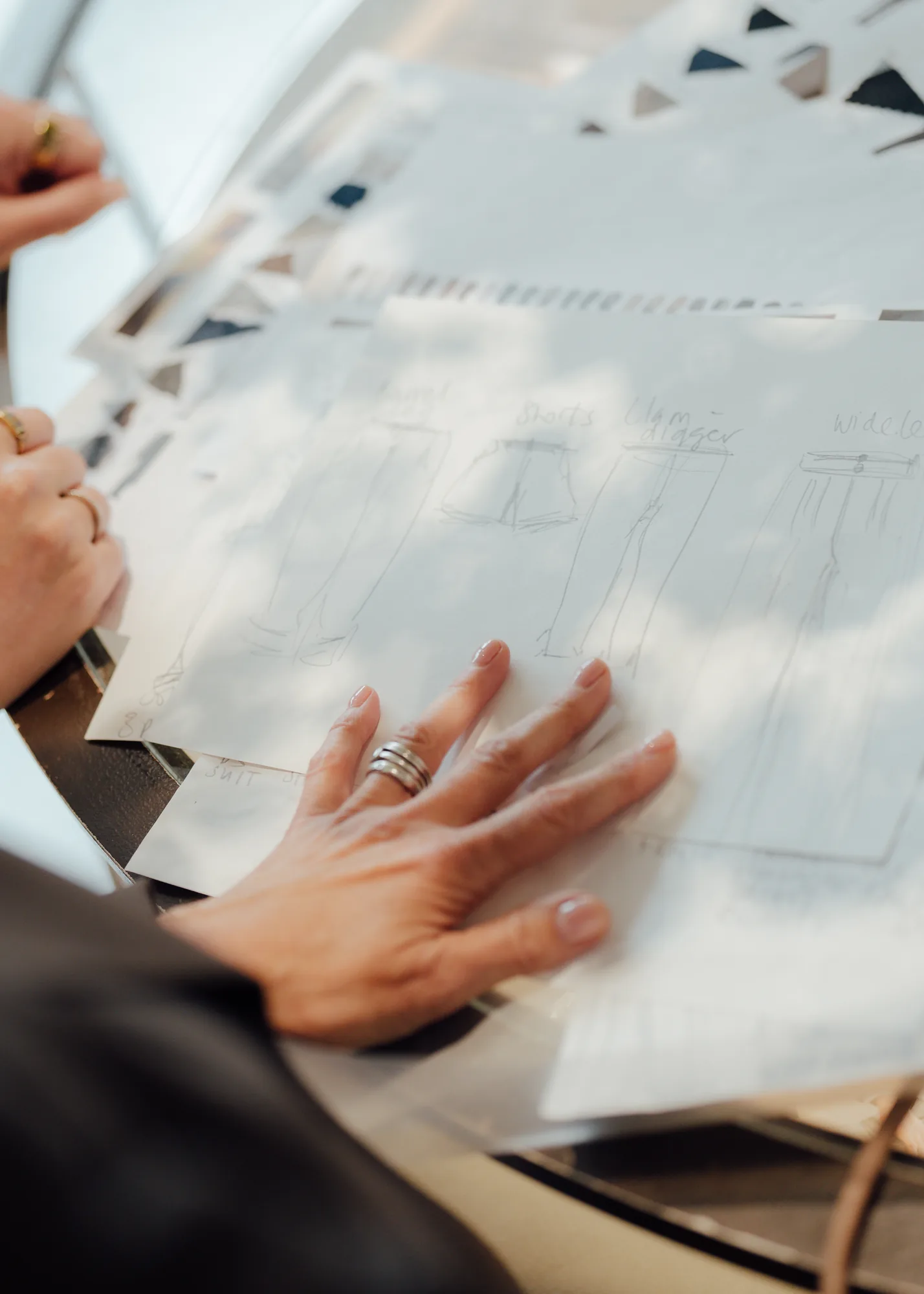 Hands reviewing hand-drawn trouser design sketches during a consultation at the Albemarle Street pop-up