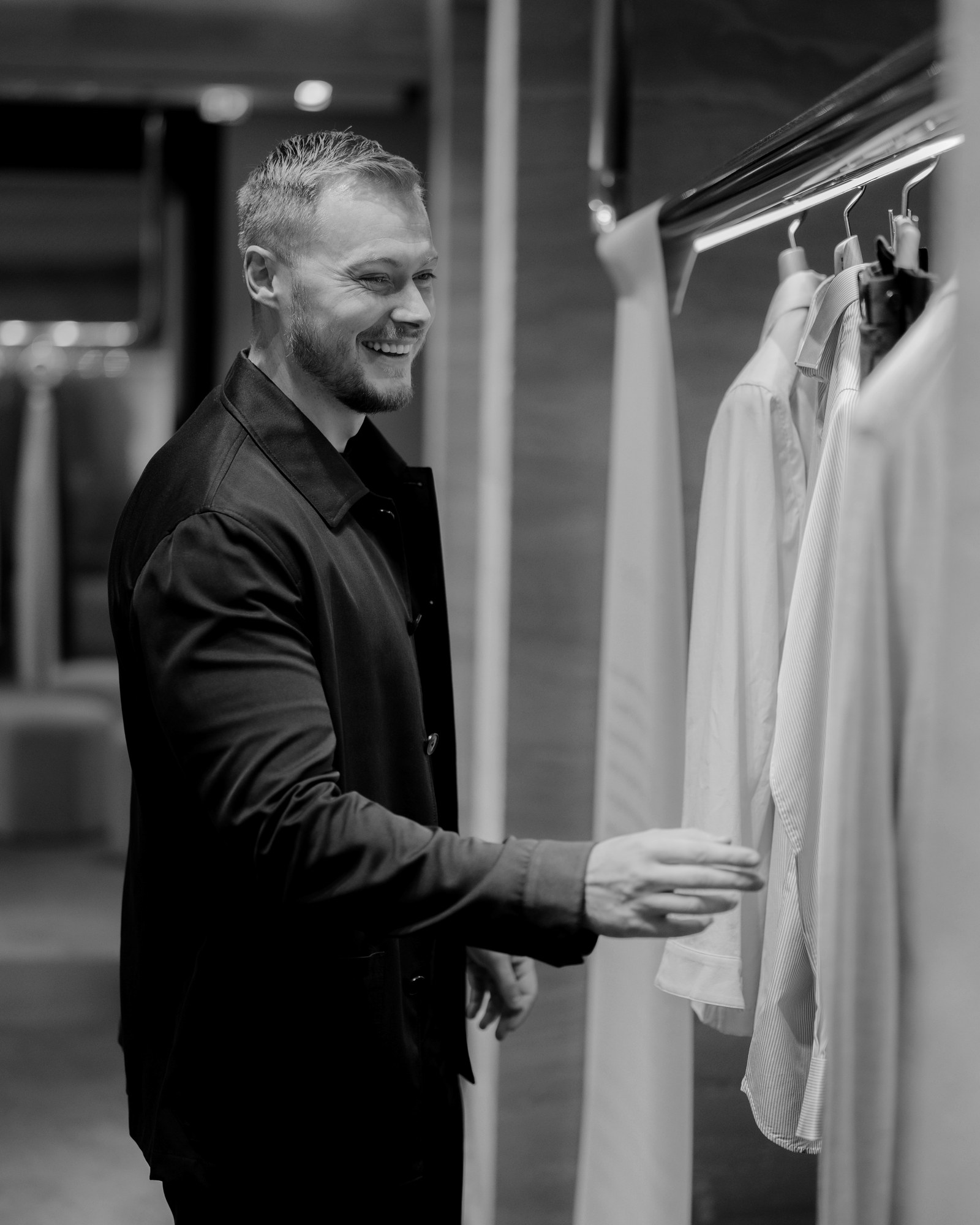 Billy Reeves, International Head Tailor, smiling beside a rail of shirts