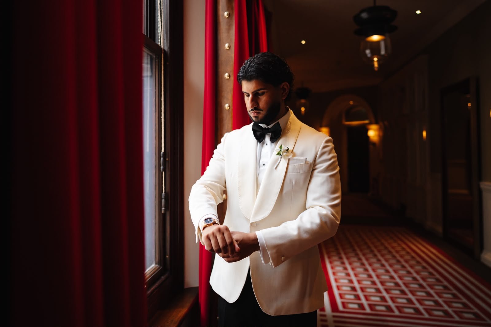 Joey in an ivory dinner jacket and black bow tie fastening his cuff in a hotel corridor