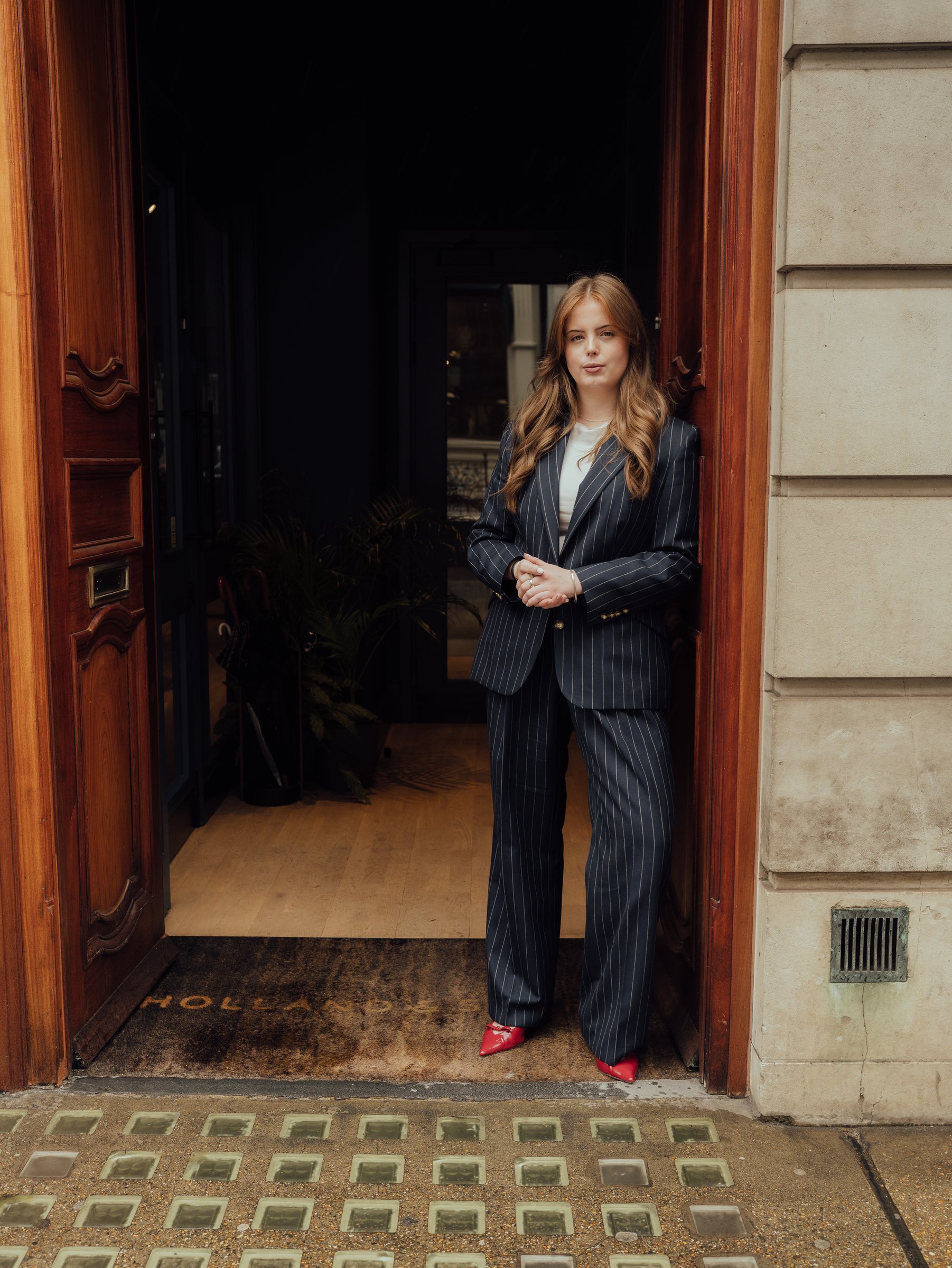 Eleanor Cook, Showroom Coordinator at Holland & Sherry, in a navy pinstripe suit at the showroom door