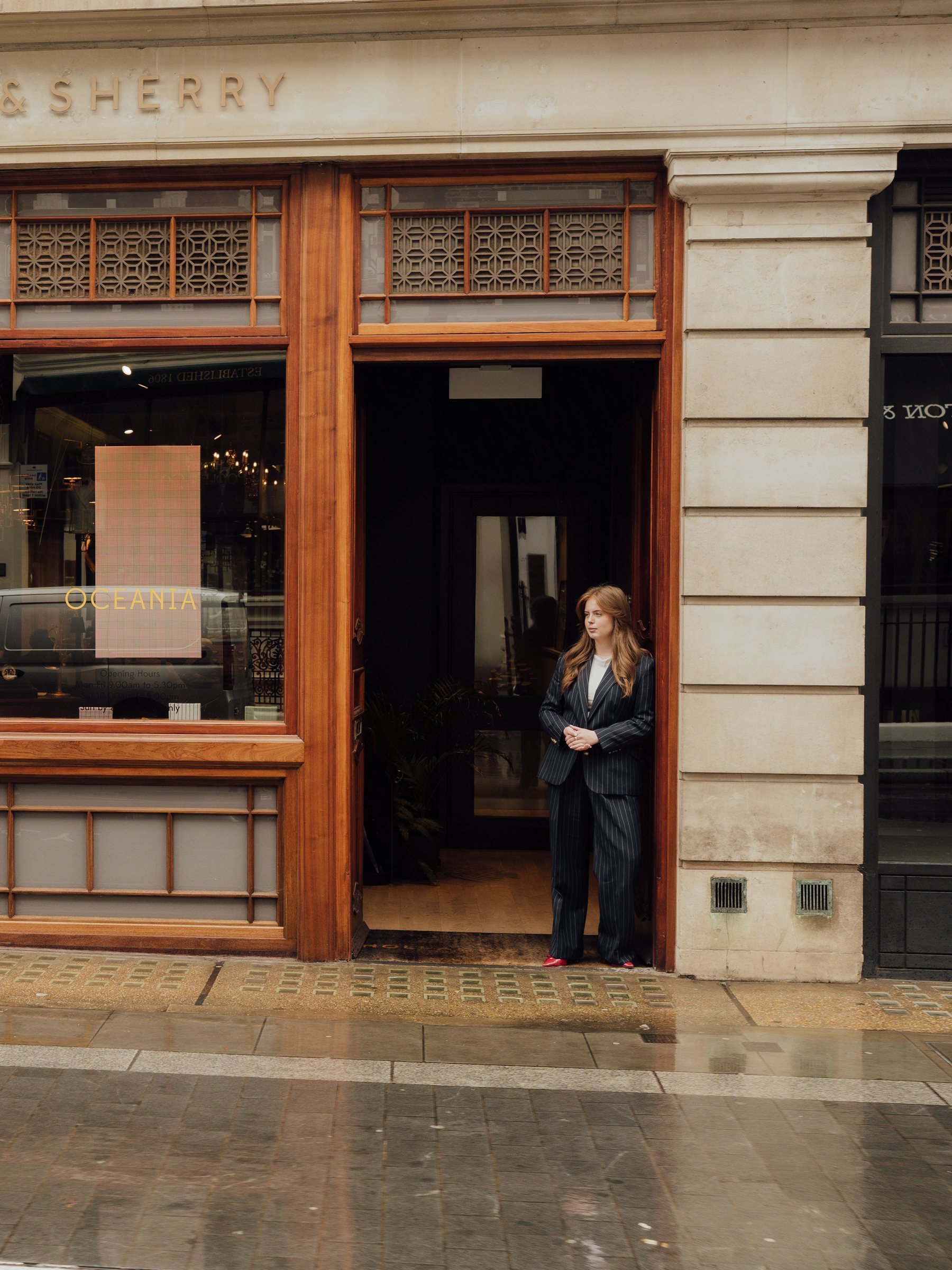 Eleanor Cook in a navy pinstripe suit standing in the doorway of the Holland & Sherry showroom in London