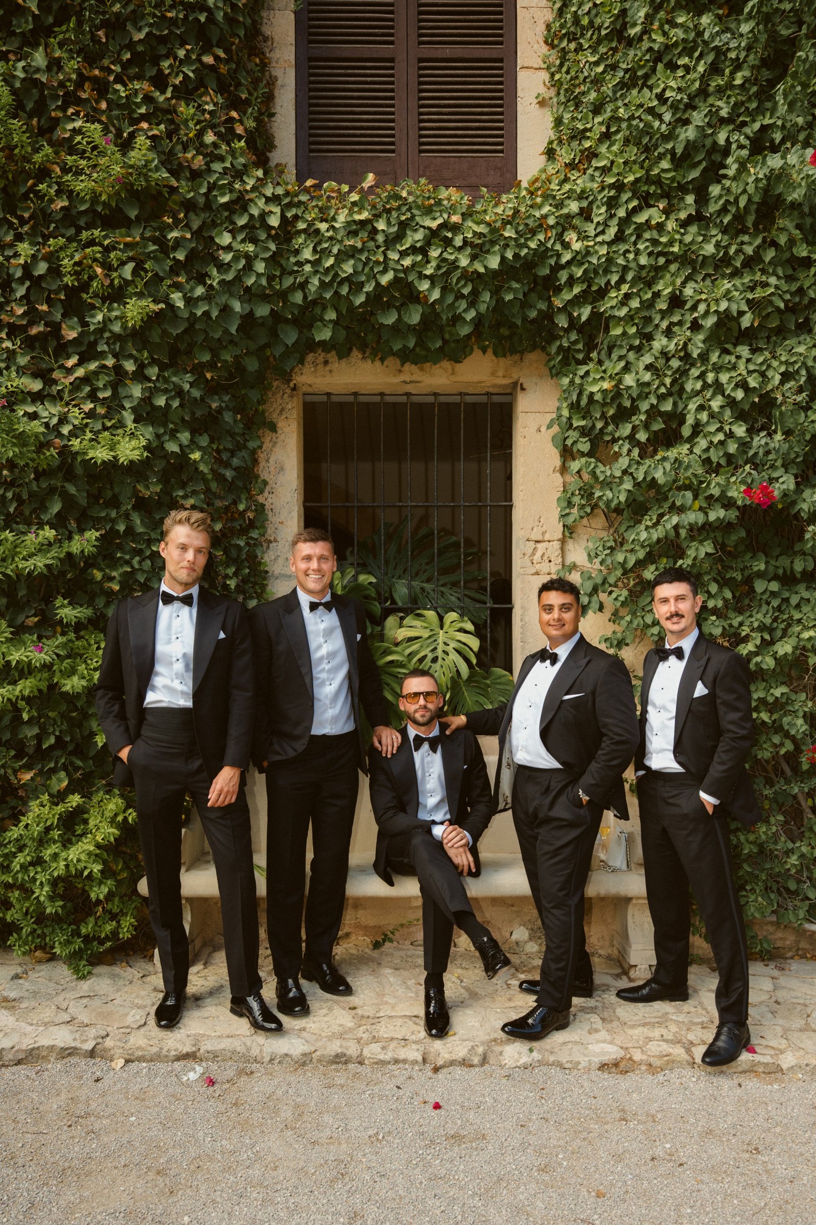 Brad and his groomsmen in black tuxedos in front of an ivy-covered wall